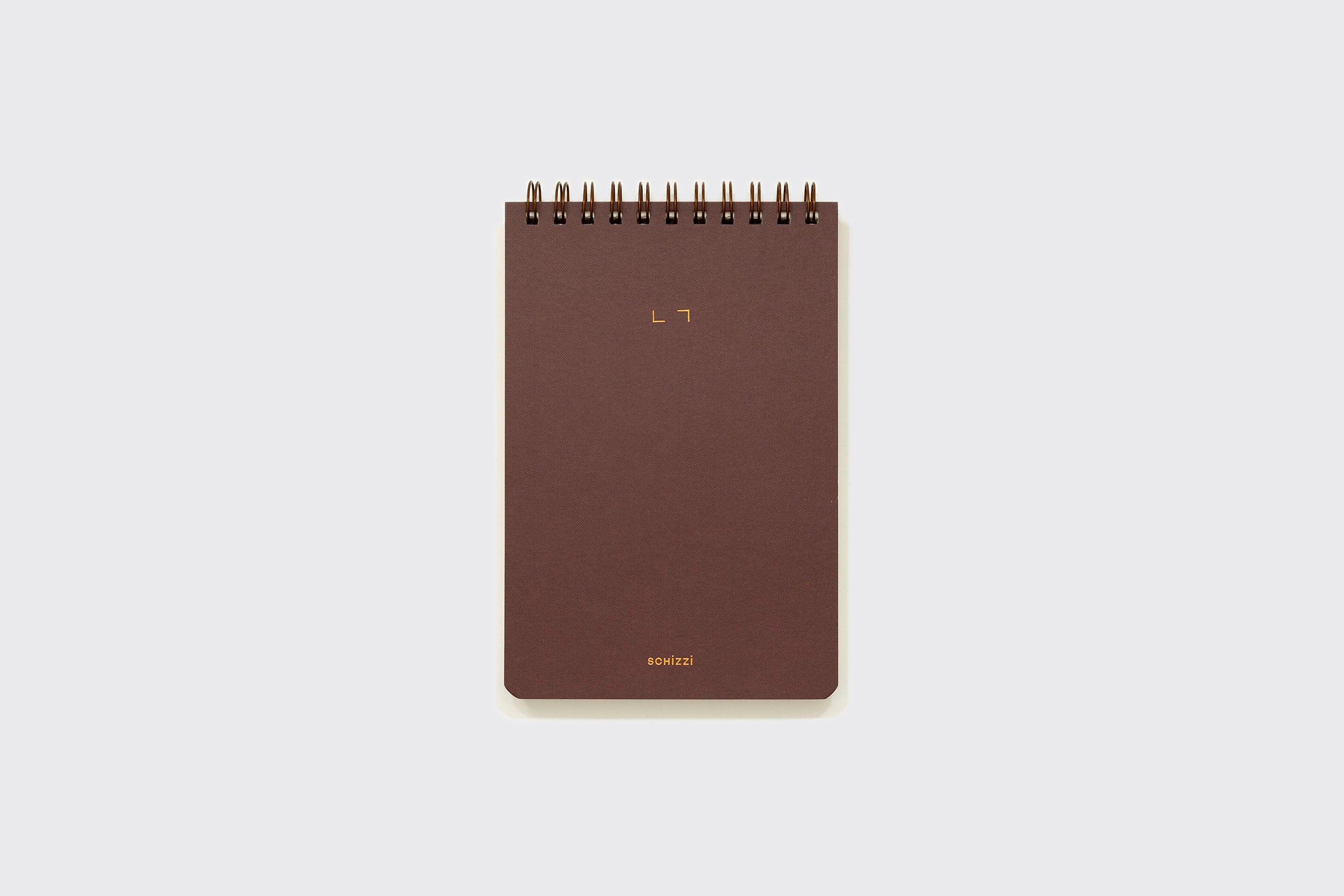Um Caderno Reporter marrom da Schizzibooks, com encadernação em espiral e cantos arredondados, está centralizado em um fundo cinza-claro liso. A capa apresenta texto dourado minimalista e é feita no Brasil com papel pólen macio.