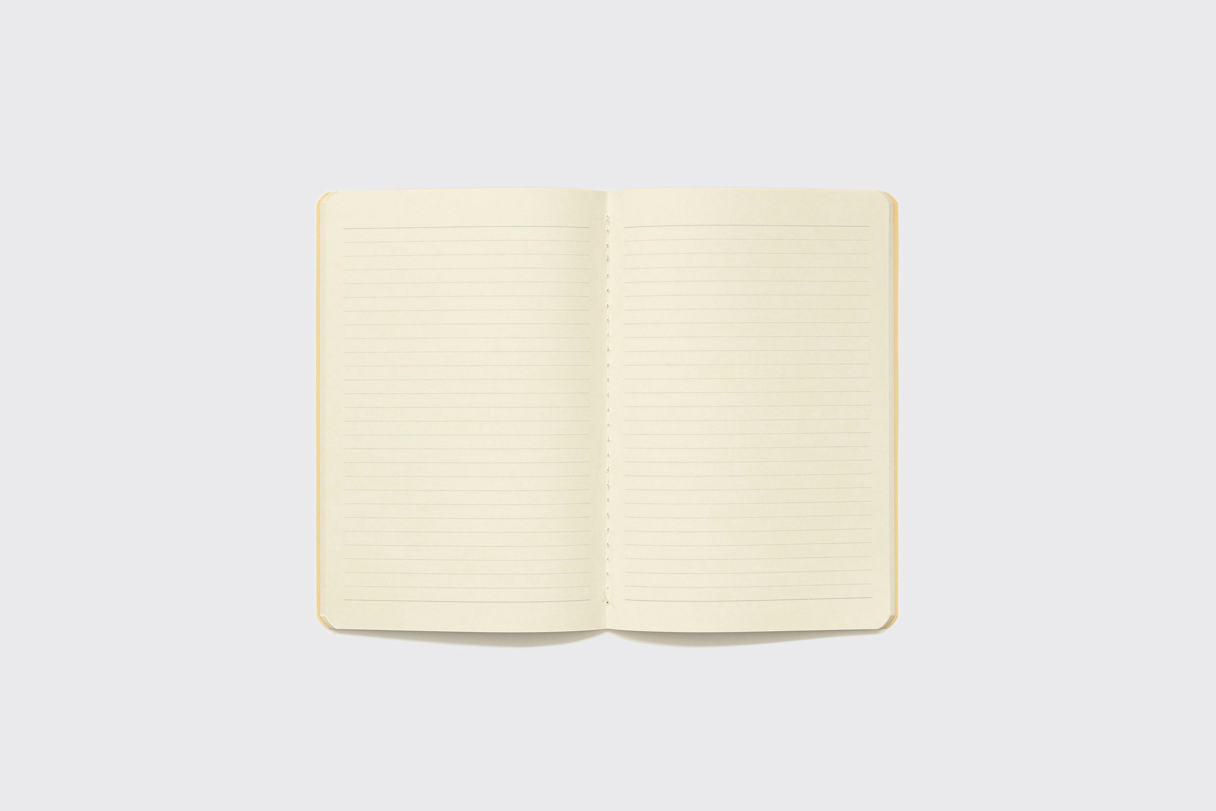 Um Caderno Flexível Schizzibooks de 15x22 cm, com páginas creme e produção artesanal brasileira, está aberto sobre um fundo cinza claro e liso.