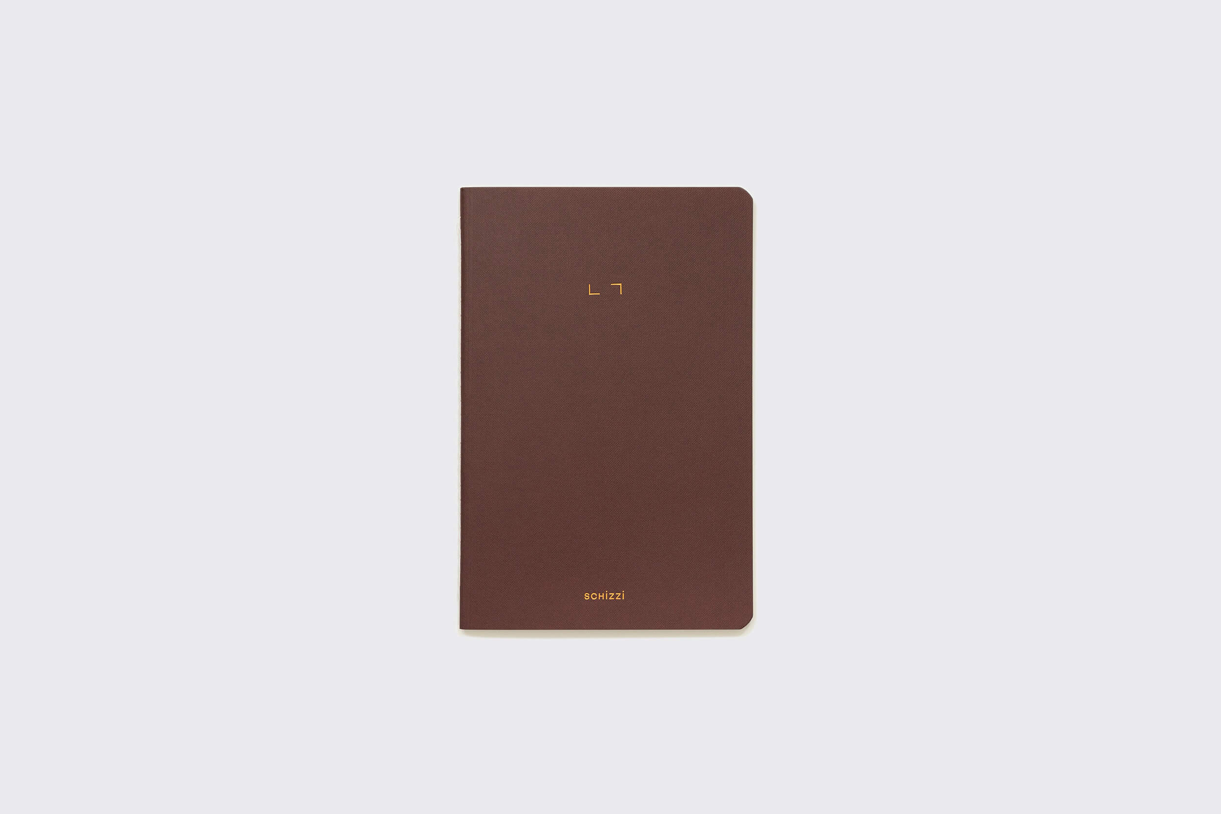 O Caderno Flexível: Savana da Schizzibooks é um caderno marrom com design minimalista e marcações elegantes na capa. Feito à mão no Brasil, ele conta com papel sem ácido para qualidade e é colocado sobre um fundo cinza claro.