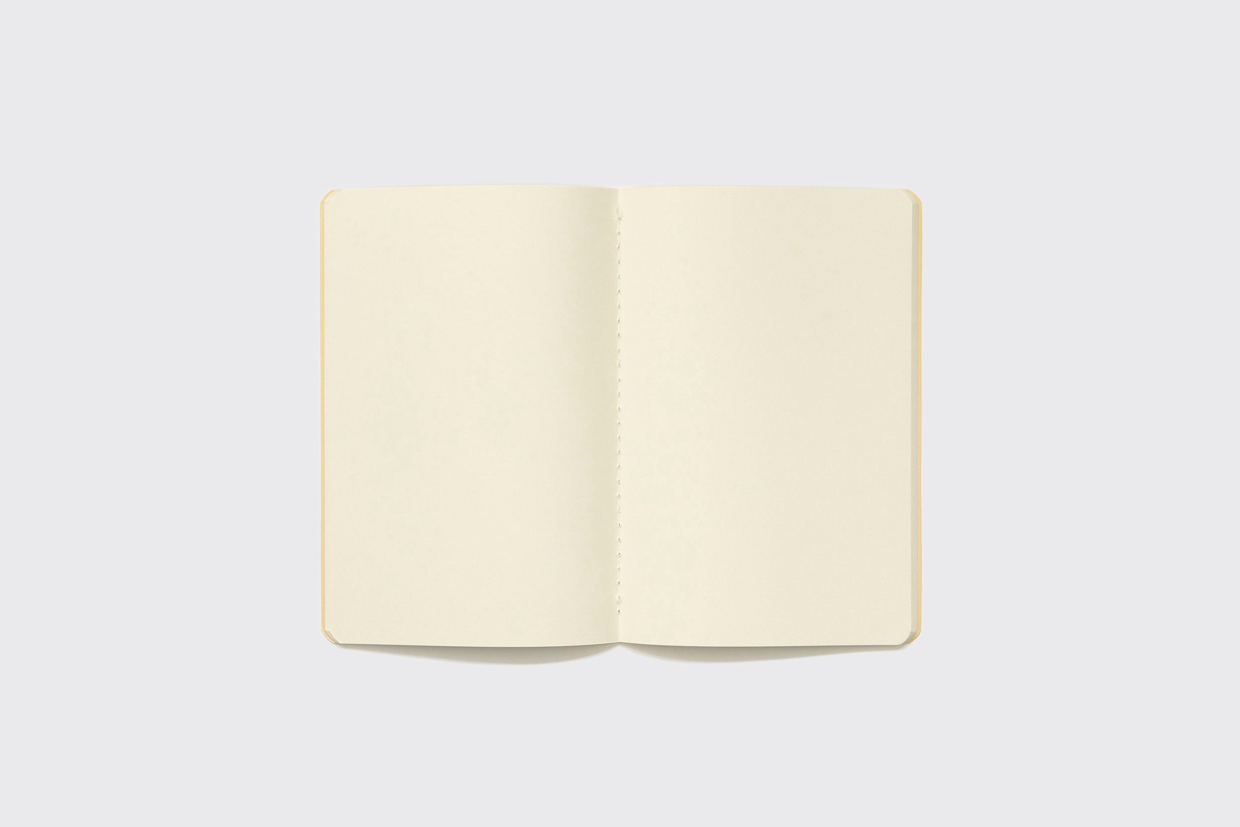 O Caderno Flexível Schizzibooks, 15x22 cm, com páginas creme, está aberto visto de cima sobre fundo cinza claro. Feito manualmente no Brasil.