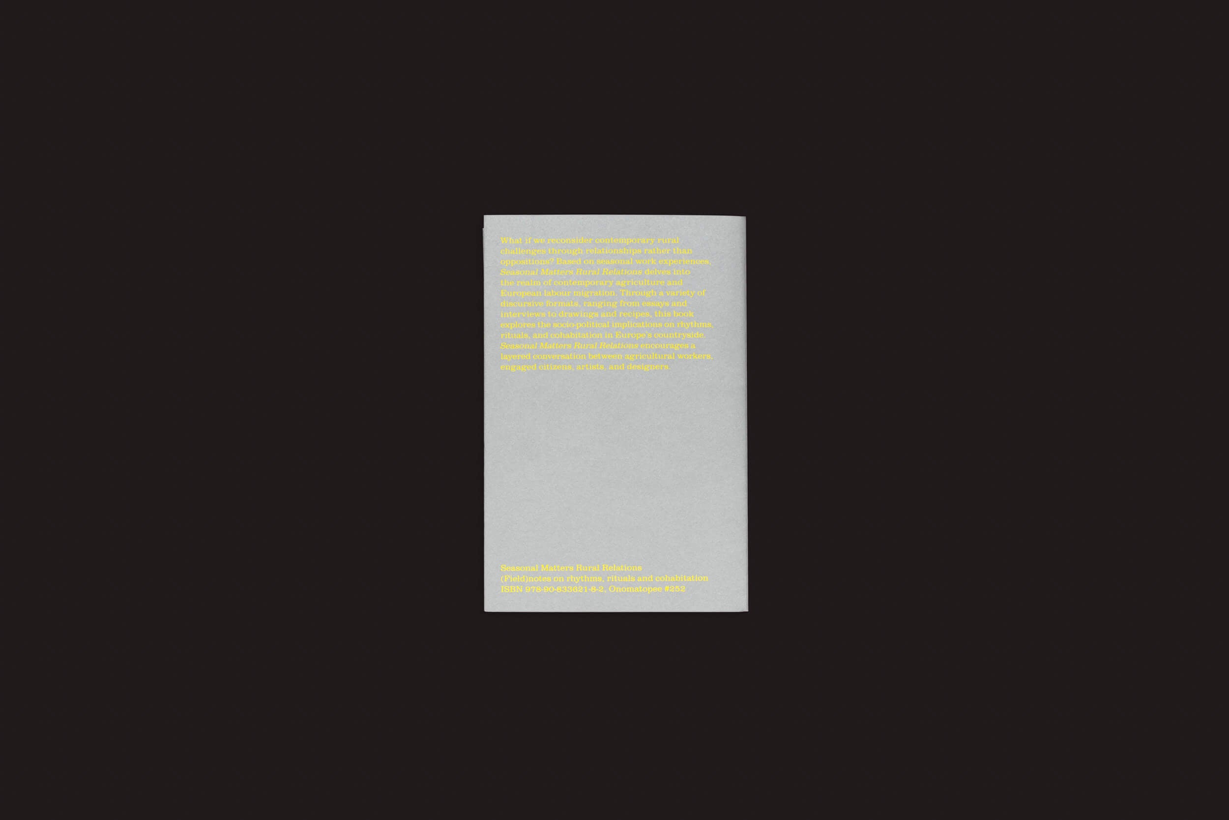 Um bloco alto, retangular e cinza claro da Onomatopee apresenta Seasonal Neighbours: Seasonal Matters Rural Relations em texto amarelo sobre um fundo preto. O pequeno texto é artisticamente centralizado no terço superior do bloco, realçando sua estética sutil.