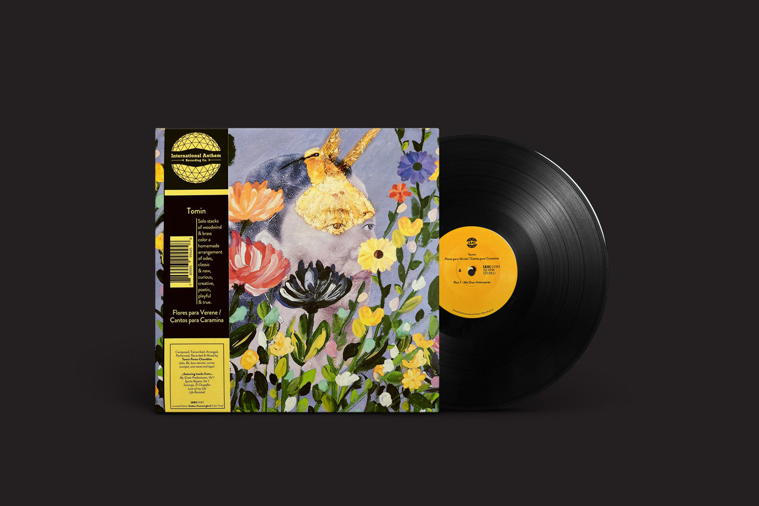 A capa do álbum "Tomin: Flores Para Verene / Cantos para Caramina" da International Anthem Recording Company exibe um design abstrato floral e de pássaros. O vinil, com uma etiqueta amarela visível, repousa sobre um fundo escuro, simbolizando o tributo melódico de um multi-instrumentista.