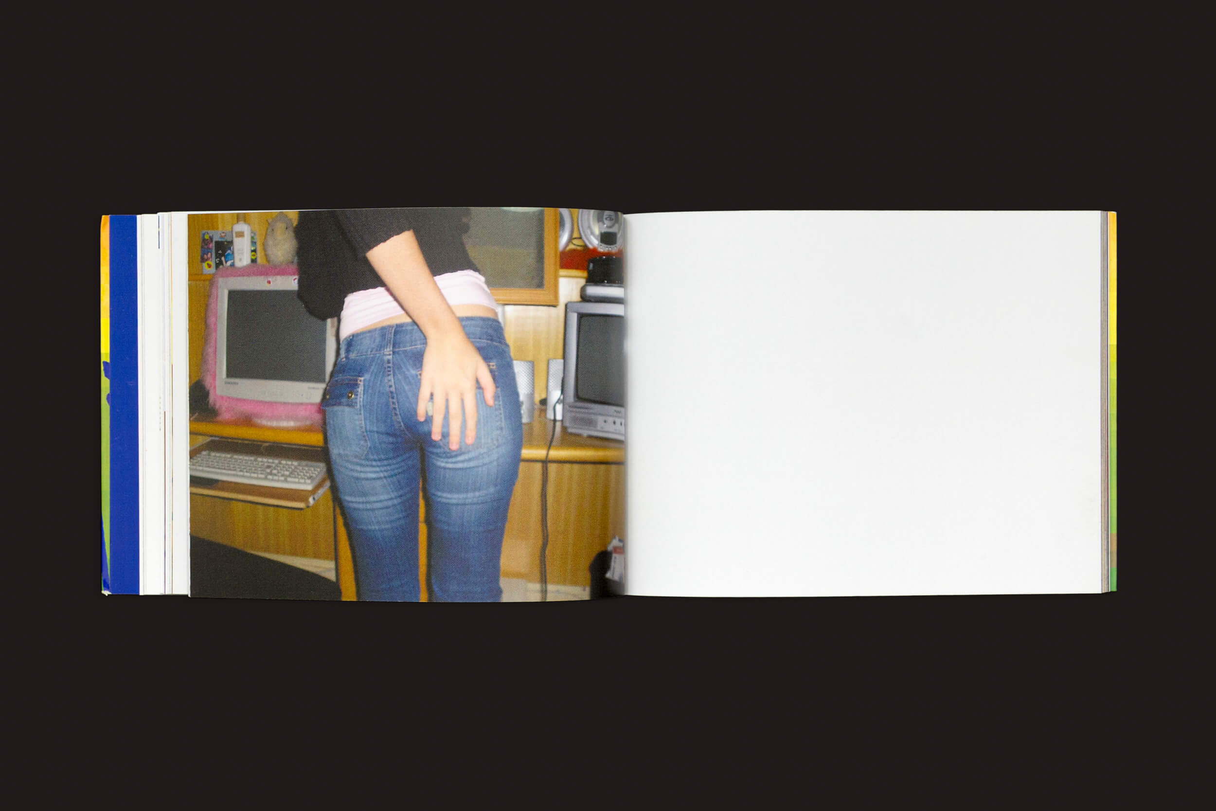 Uma página de *Amanda Devulsky: Ultrasuperfície* da zero-Edições mostra uma artista de jeans azul e blusa preta perto de uma mesa, com a mão no bolso. A mesa abriga um monitor de moldura rosa estilo vintage, ecoando o Fotolog.net; a página oposta está em branco.