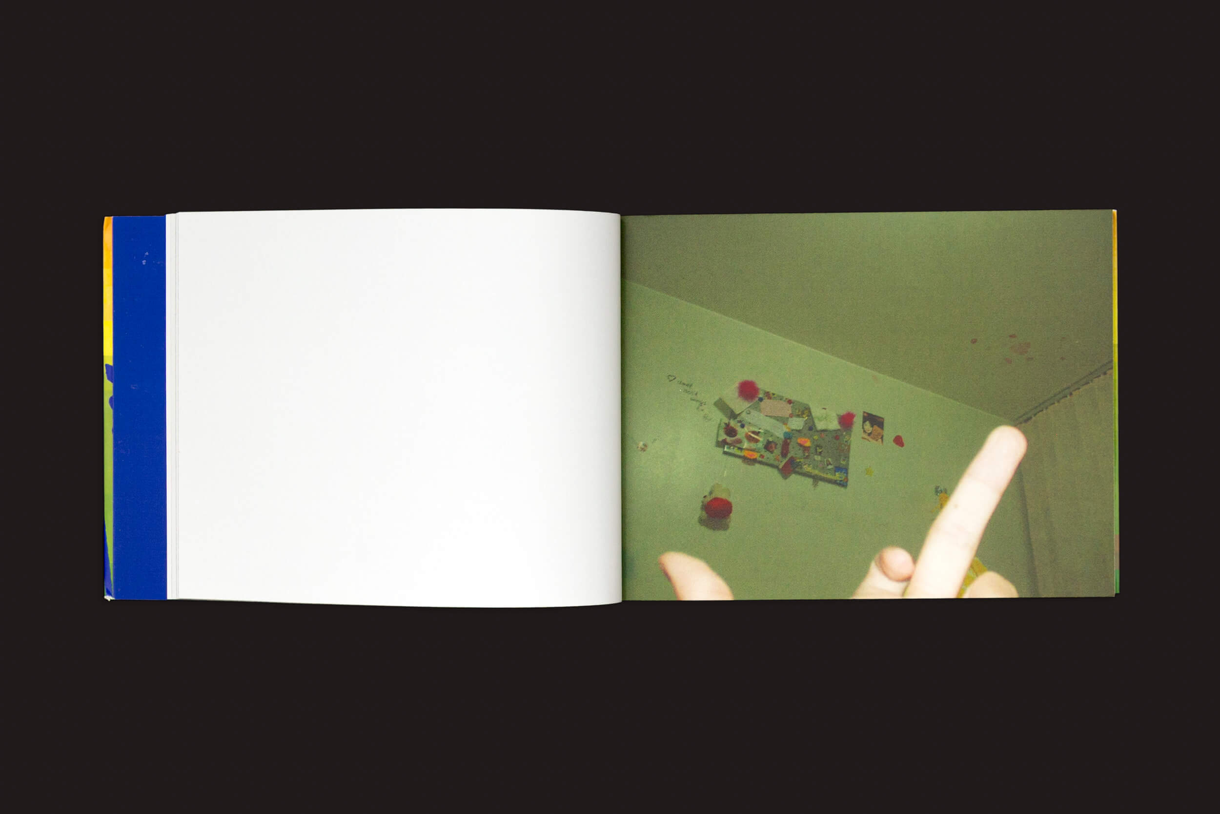 Um livro aberto sobre uma superfície escura captura a essência de Amanda Devulsky: Ultrasuperfície da zero-Edições. A página da esquerda está em branco, enquanto a da direita apresenta uma foto de uma sala com decorações ultrasuperfície e uma mão gesticulando rudemente, ecoando a autenticidade crua do Fotolog.net.