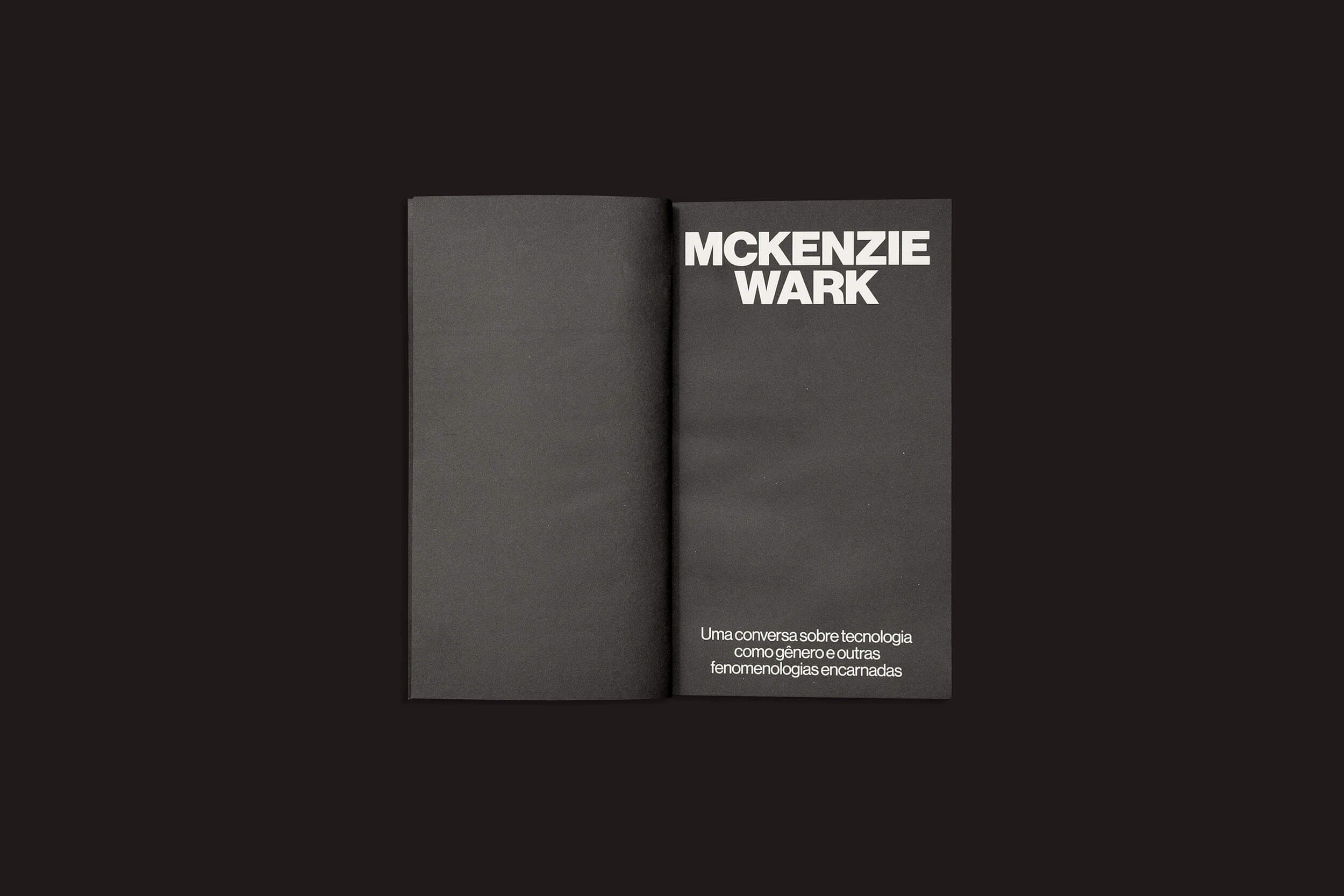 Livro aberto, de capa preta, sobre fundo preto, com a inscrição "MCKENZIE WARK" em grandes letras brancas na página direita e legenda em português: "Uma conversa sobre tecnologia como gênero e outras fenomenologias encarnadas", de sobinfluencia.