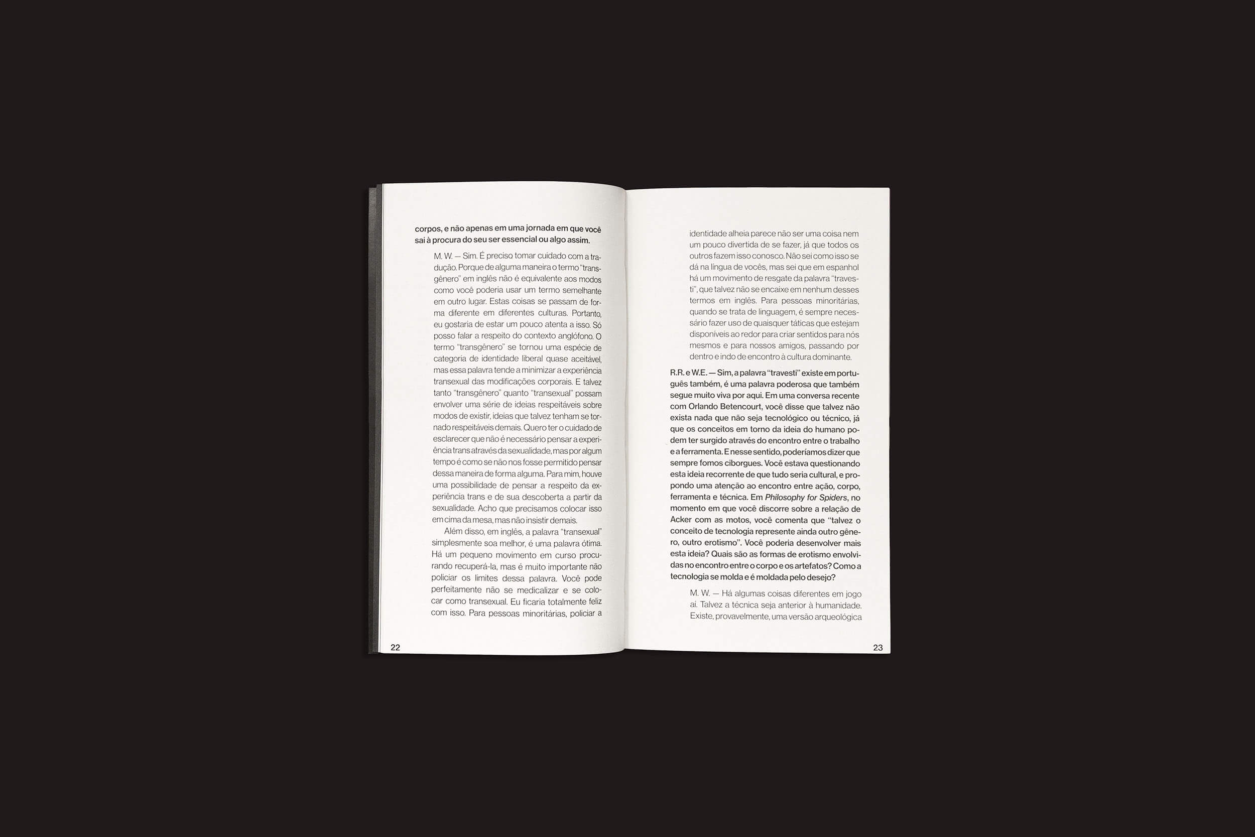 Um livro aberto sobre fundo preto revela as páginas 22 e 23 repletas de parágrafos envolventes em fonte serifada, discutindo o marxismo e os modos de produção. Intitula-se "Mckenzie Wark: Uma conversa sobre tecnologia como gênero e outras fenomenologias encarnadas" de sobinfluência.