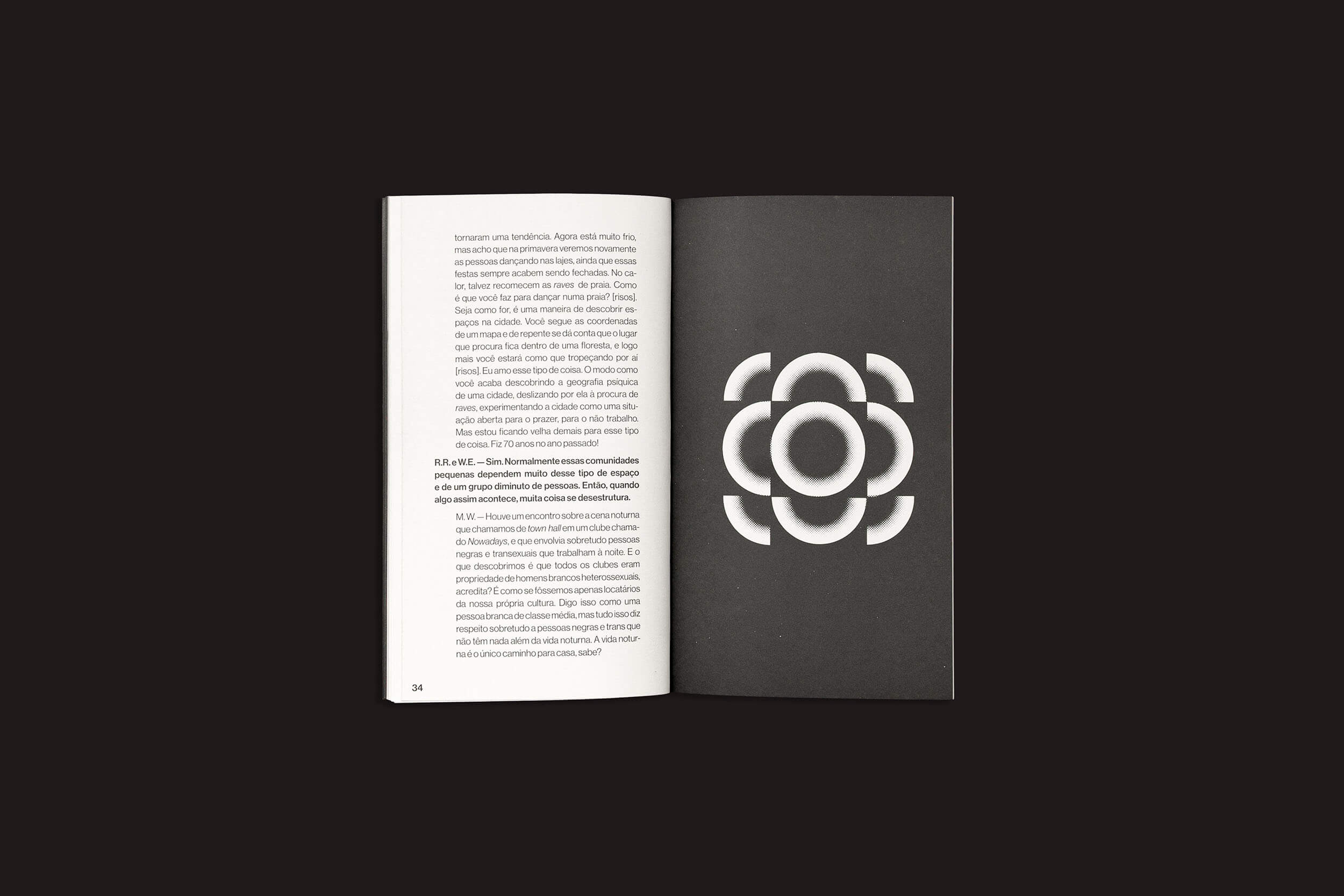 Um livro aberto da sobinfluencia repousa sobre uma superfície escura. A página da esquerda mostra um texto em português discutindo nuances do marxismo, enquanto a da direita exibe uma flor branca estilizada com pétalas sobrepostas contra um fundo preto. O produto é intitulado "Mckenzie Wark: Uma conversa sobre tecnologia como gênero...