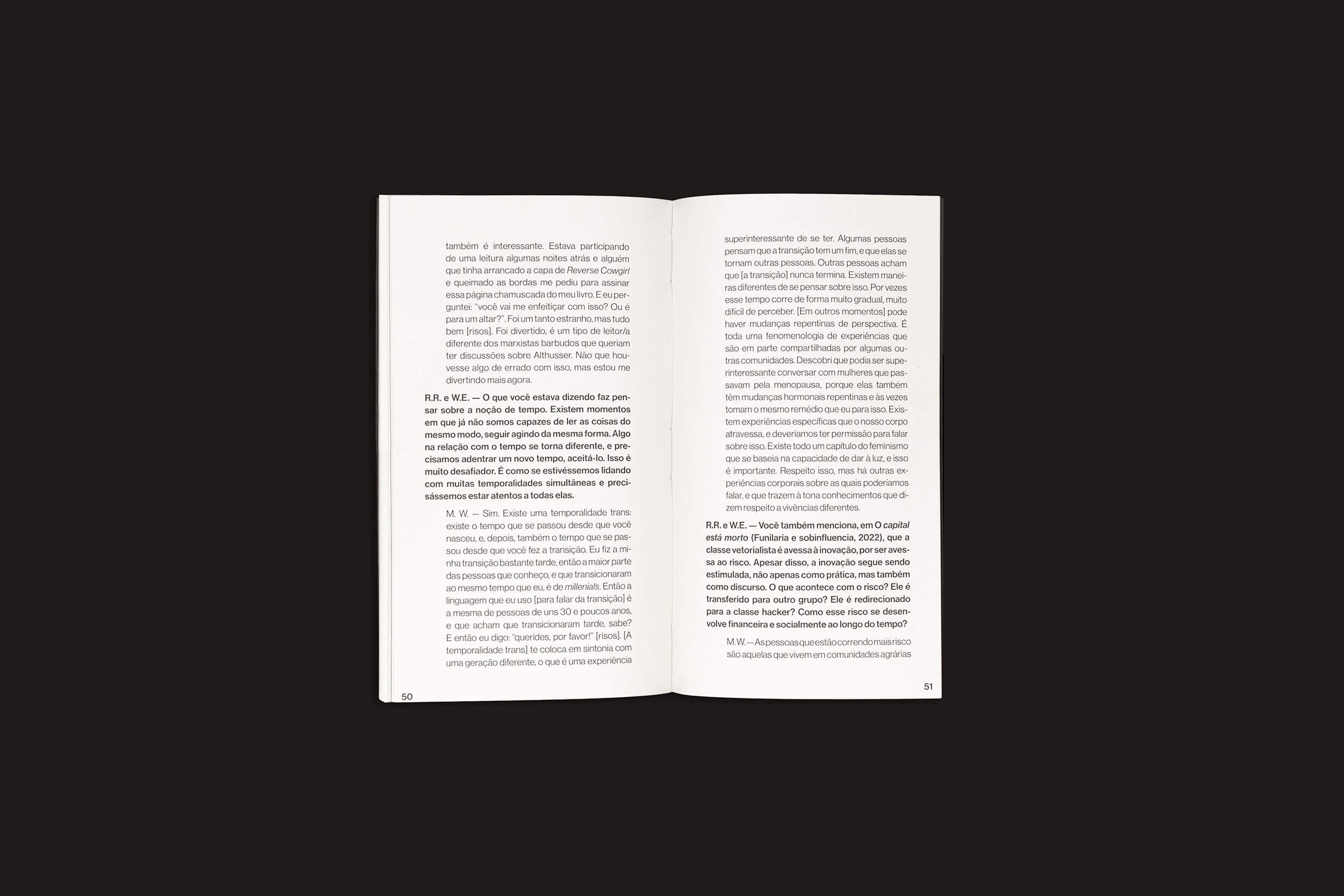 Um livro aberto sobre superfície escura mostra as páginas 50 e 51, repletas de denso texto serifado que lembra uma entrevista ou diálogo sobre o impacto da linguagem nos modos de produção. O livro, intitulado “Mckenzie Wark: Uma conversa sobre tecnologia como gênero e outras fenomenologias encarnadas”, é de sobinfluência.