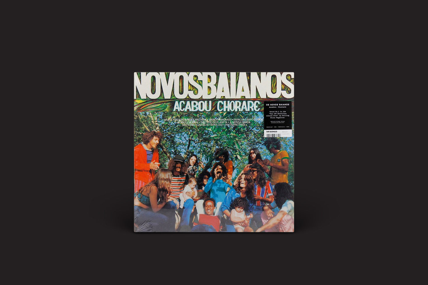 A capa do álbum Novos Baianos: Acabou Chorare, do Mr Bongo, mostra a banda ao ar livre, embaixo de uma árvore, interagindo alegremente, com cores vibrantes e o título do álbum em letras brancas e verdes em negrito acima.