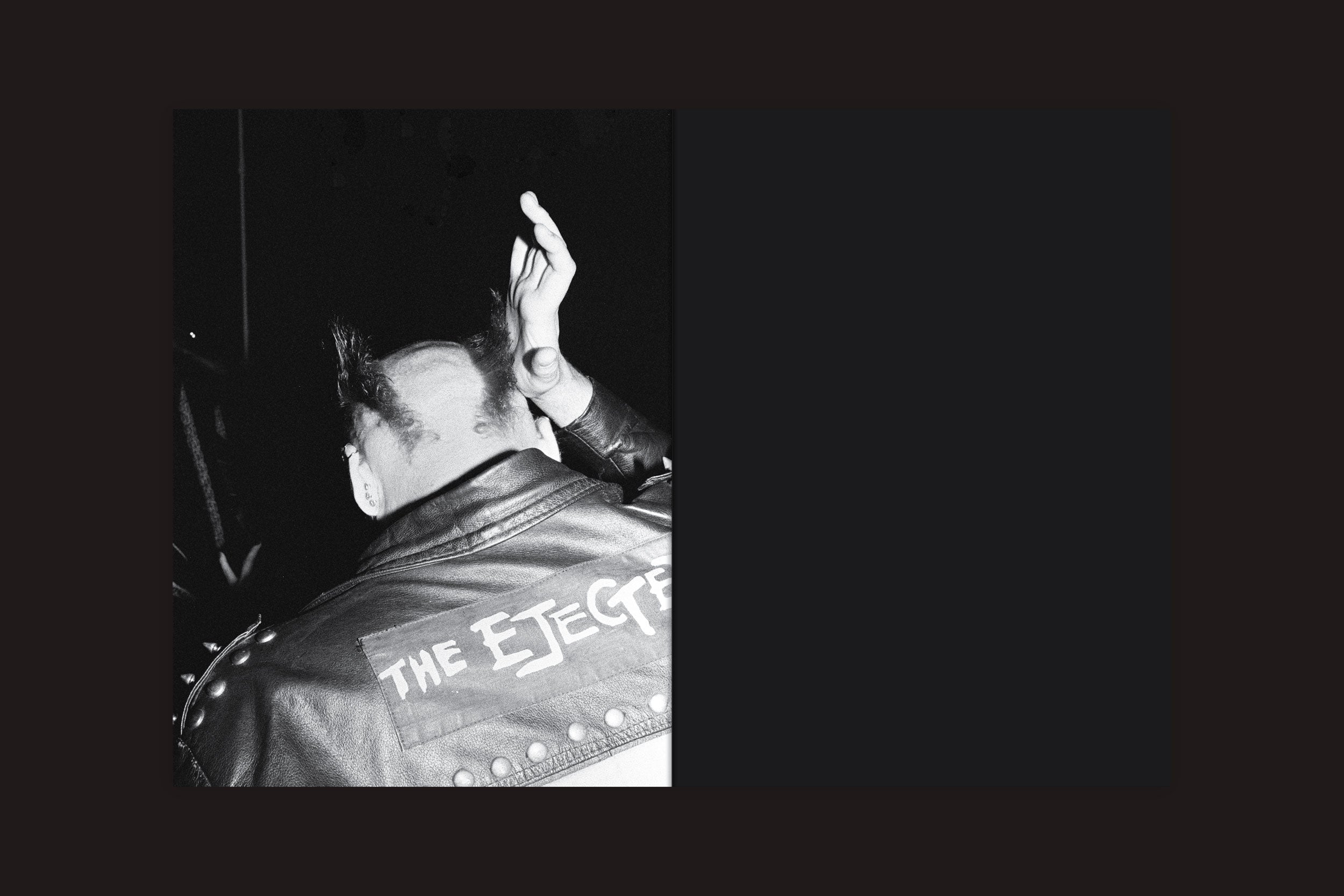Foto em preto e branco de uma pessoa com moicano, vista por trás em uma jaqueta com tachas, ergue o punho em sinal de desafio. As sombras evocam a obra de Selo Turvo "André Djanikian: Algunos sentimientos no cambian junto a las estaciones.