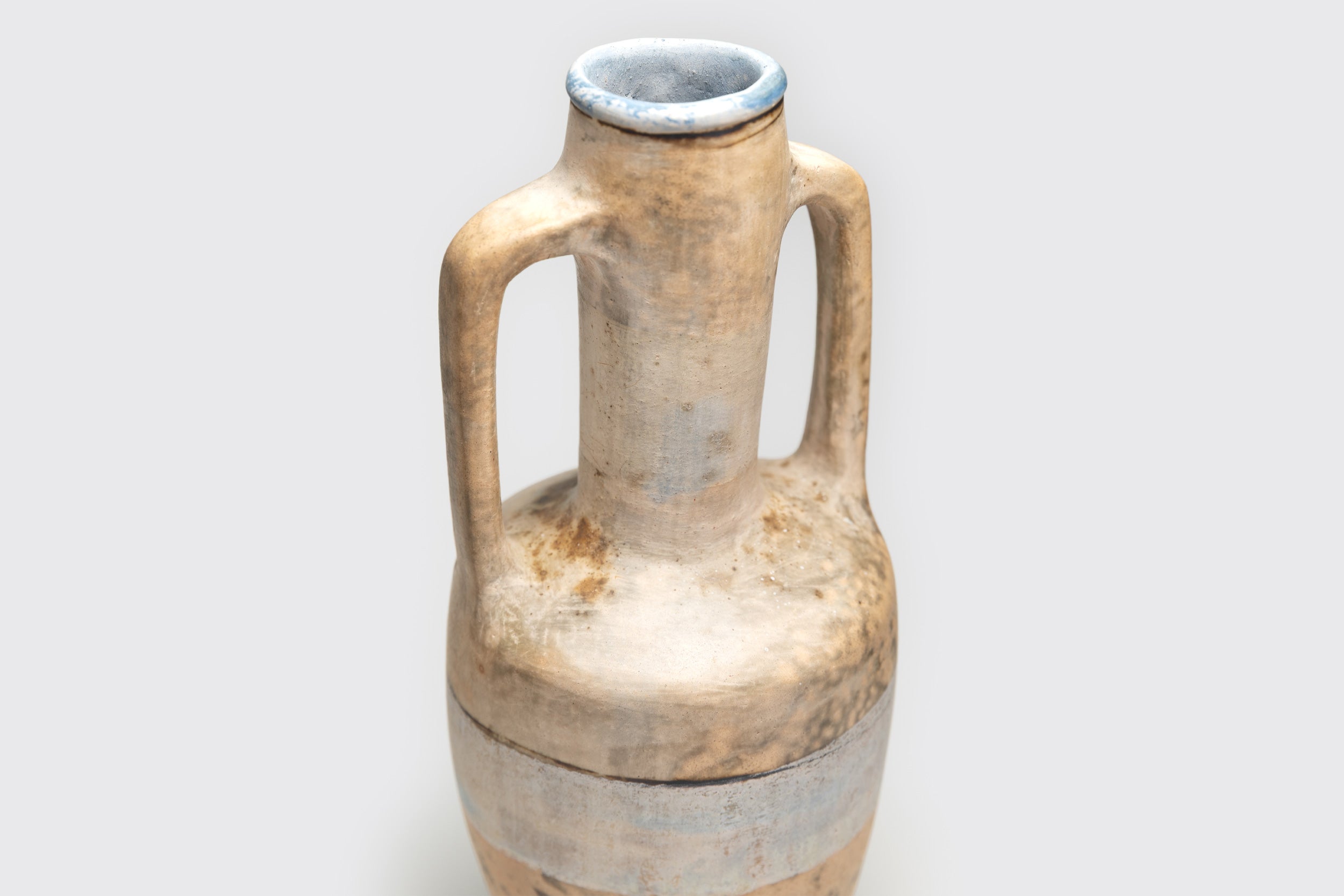 O Ânfora#1 de Derek Tasker-Norton é um vaso de cerâmica com duas alças e gargalo estreito, com acabamento artesanal rústico em bege e azul claro para um visual antigo, sobre um fundo cinza claro simples.