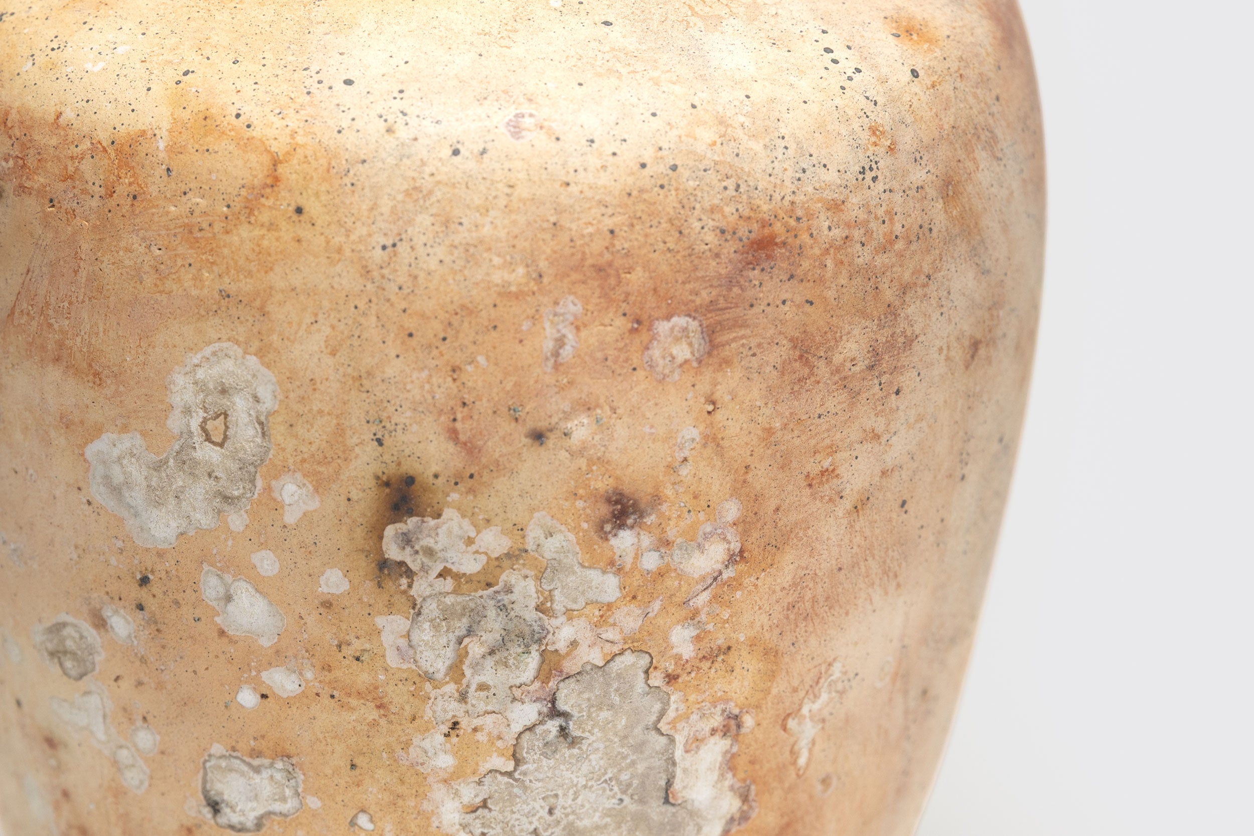 Close-up de Ânfora nº 3 de Derek Tasker-Norton: um vaso de cerâmica artesanal marrom-claro, texturizado e envelhecido, com manchas brancas e cinzas sugerindo idade ou depósitos minerais. Fundo liso e claro.