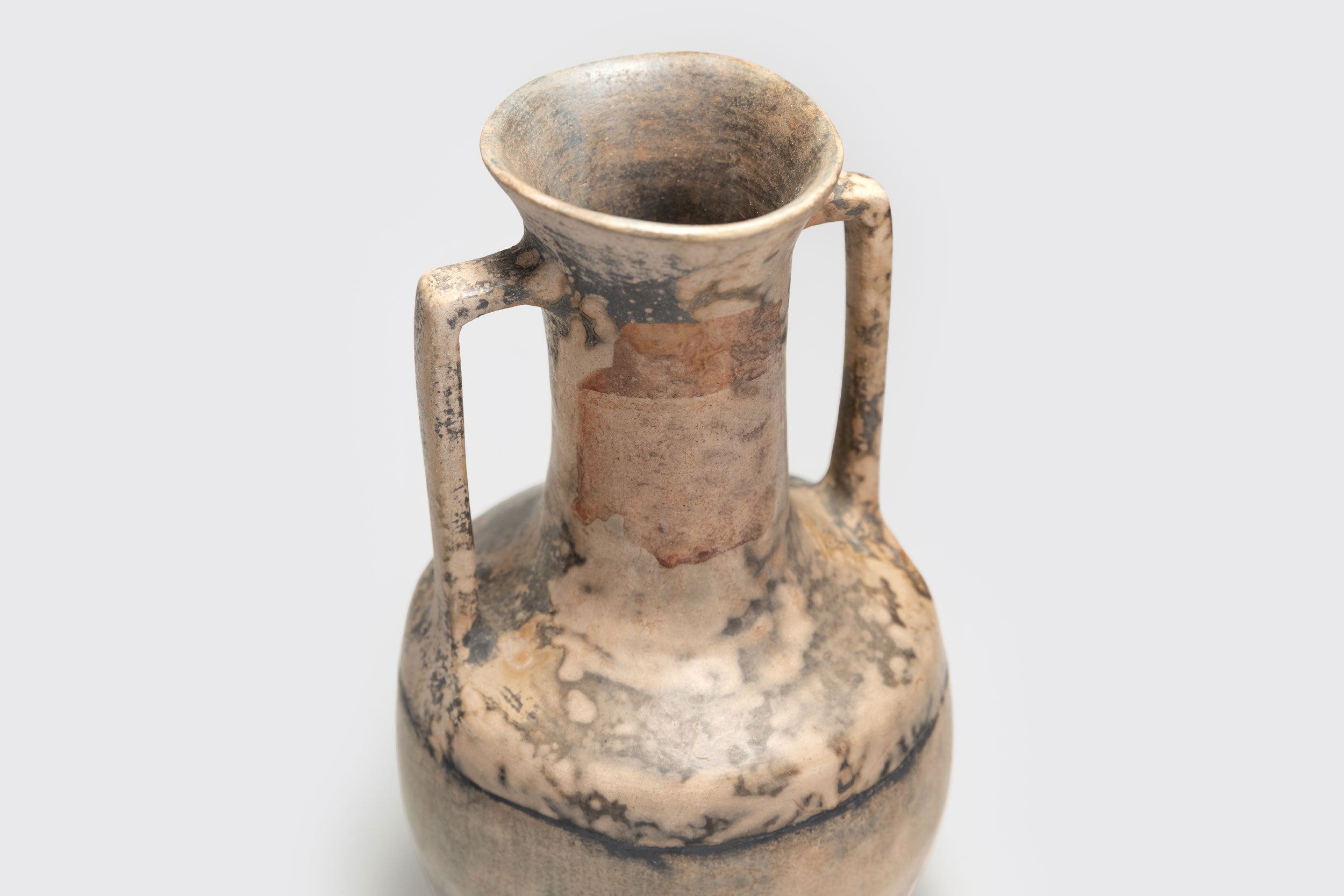 A Ânfora#4 de Derek Tasker-Norton é um vaso artesanal de pescoço estreito, corpo largo e duas alças verticais, com acabamento rústico em padrões moteados bege, marrom e cinza que remetem à antiguidade.