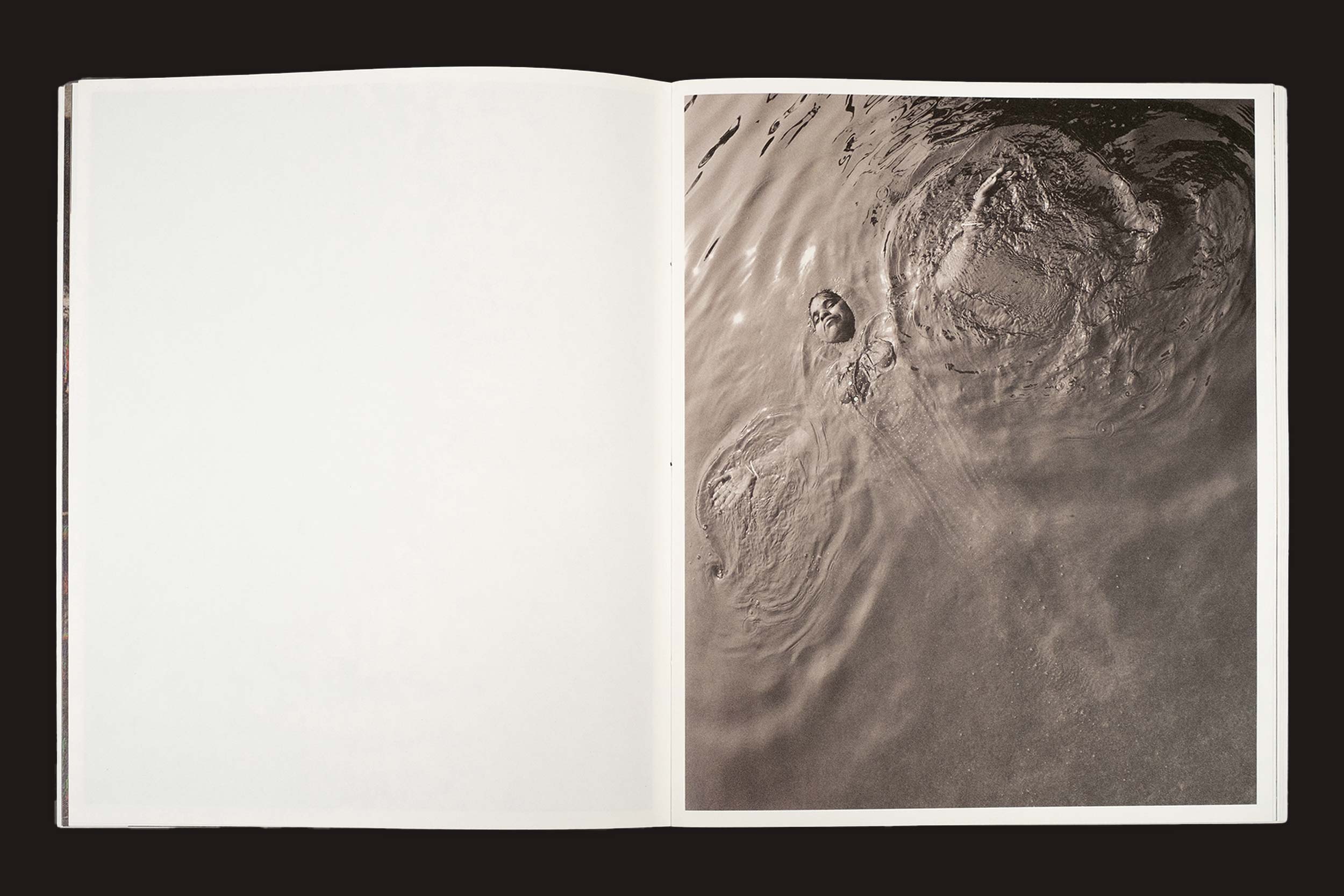 Uma cópia aberta de "Bharat Sikka: Ripples in the Pond", da Fw:Books, mostra uma página esquerda em branco e, à direita, uma foto em tom sépia de uma investigação visual: uma pessoa flutua de costas em lagos tranquilos, com suaves ondulações ao seu redor.