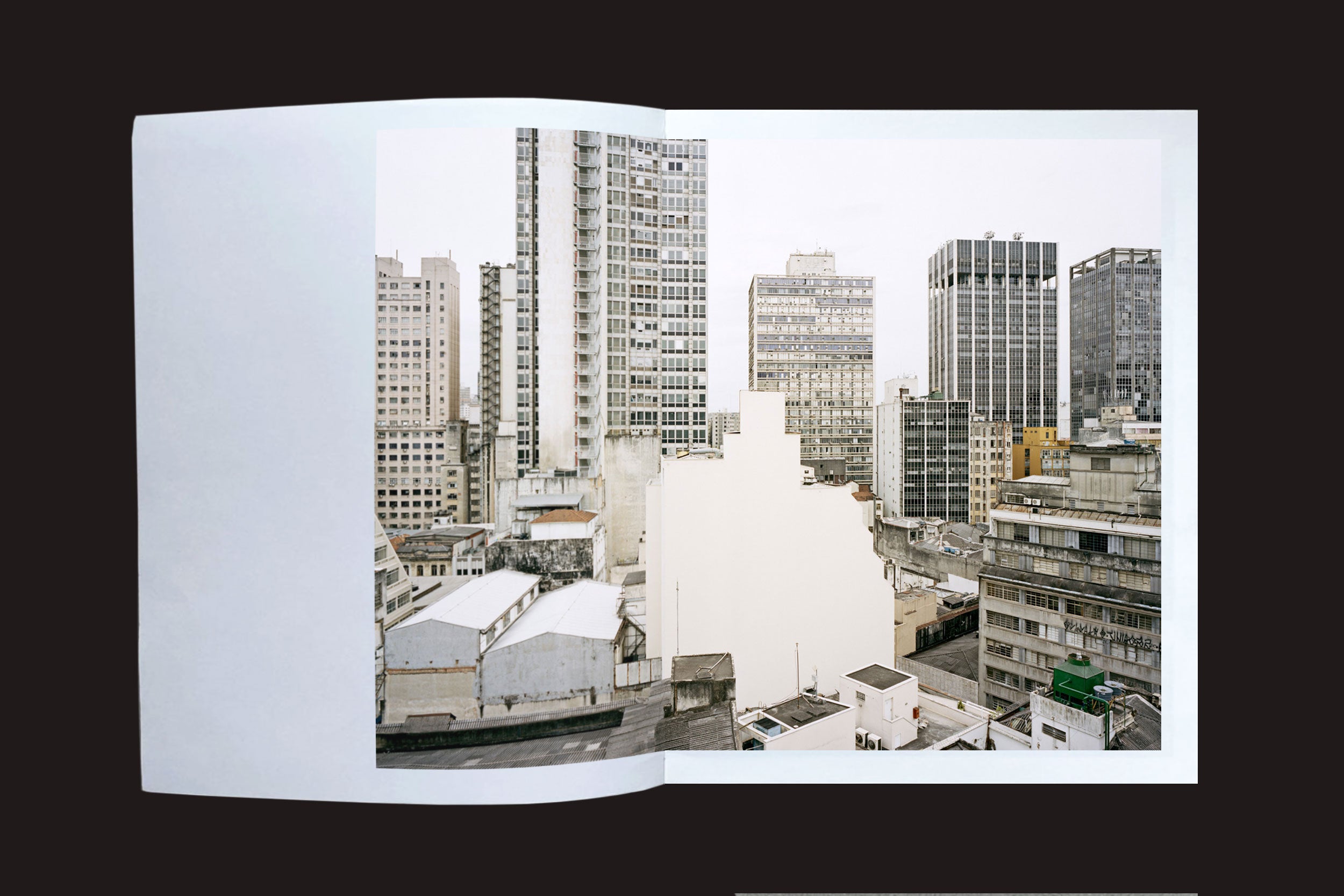 Um livro aberto de Felipe Russo: Centro by Auto-edição mostra uma paisagem urbana de edifícios altos, com uma grande área em branco no centro obscurecendo algumas estruturas, criando contraste com a arquitetura de São Paulo.