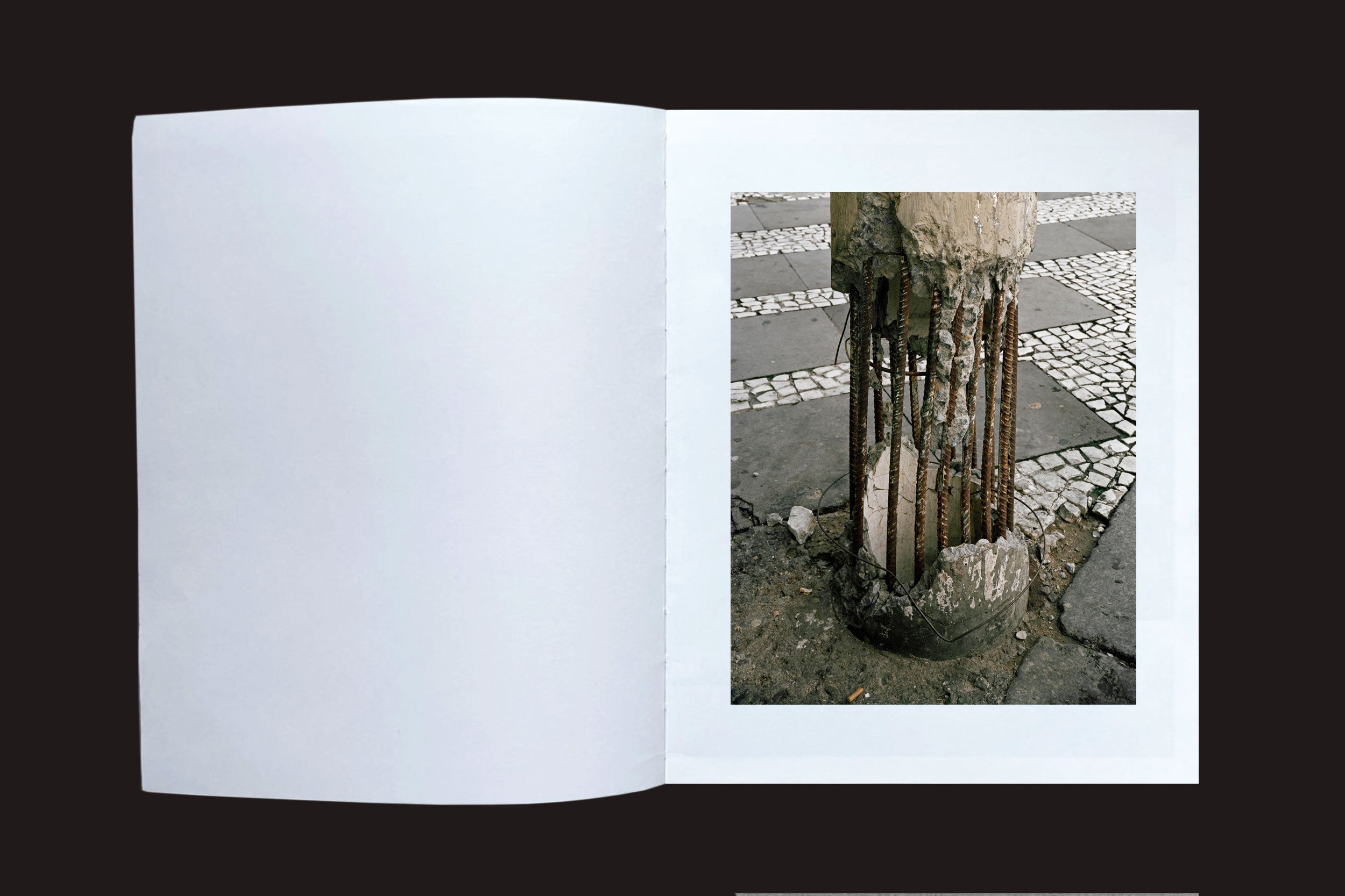 A fotografia urbana do livro "Felipe Russo: Centro" (Auto-edição) mostra uma página com um poste de concreto danificado e vergalhões expostos sobre ladrilhos, tendo faixa de pedestres ao fundo no Centro de São Paulo.