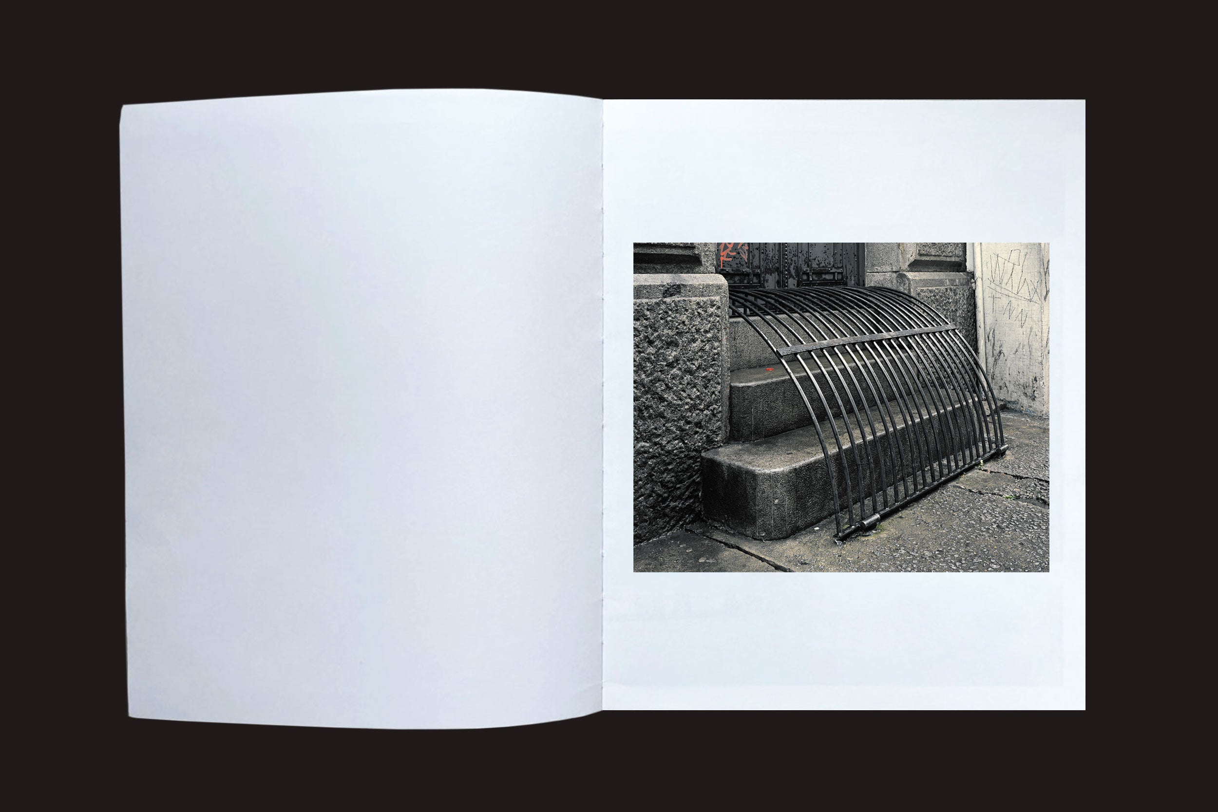 Um livro aberto de Felipe Russo: Centro by Auto-edição mostra uma fotografia urbana de uma grade de metal em degraus de concreto do lado de fora de um prédio, em um fundo branco com borda preta, destacando a paisagem urbana única do Centro de São Paulo.