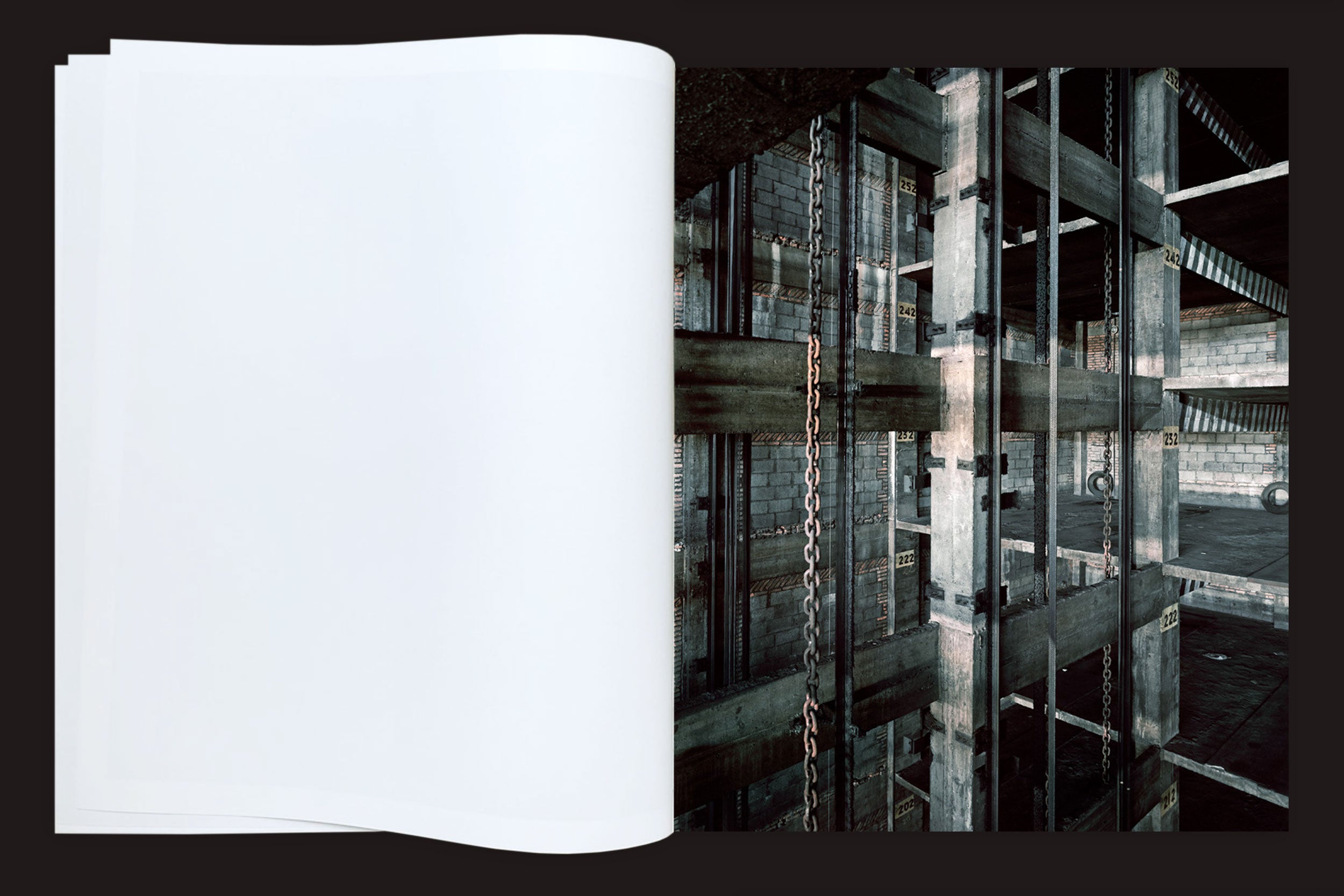 O livro aberto "Felipe Russo: Garagem Automática", da Auto-edição, mostra páginas em branco à esquerda e uma fotografia arquitetônica de um edifício de concreto garagem automatizado em construção à direita, sobre um fundo preto.