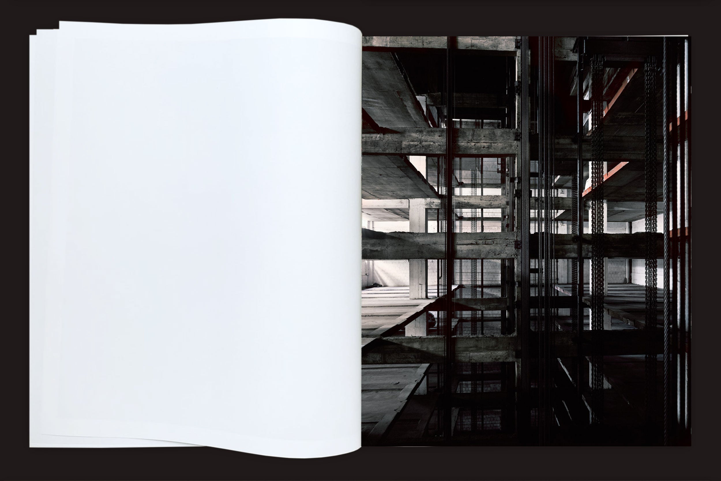 Um livro aberto, Felipe Russo: Garagem Automática by Auto-edição, mostra uma página esquerda em branco e, à direita, uma fotografia arquitetônica de um prédio de concreto inacabado em São Paulo, com vigas expostas e sombras geométricas.