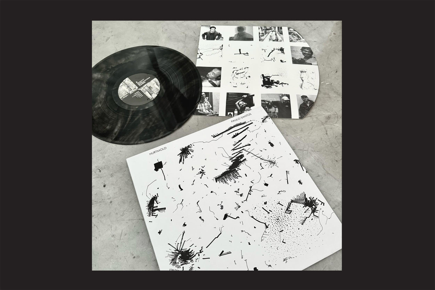 Curado by Hurtmold & Paulo Santos (Nada Nada Discos): um vinil preto marmorizado com uma capa de esboços/fotos em preto e branco e uma capa externa com arte abstrata preta minimalista, refletindo seu estilo único de música instrumental.