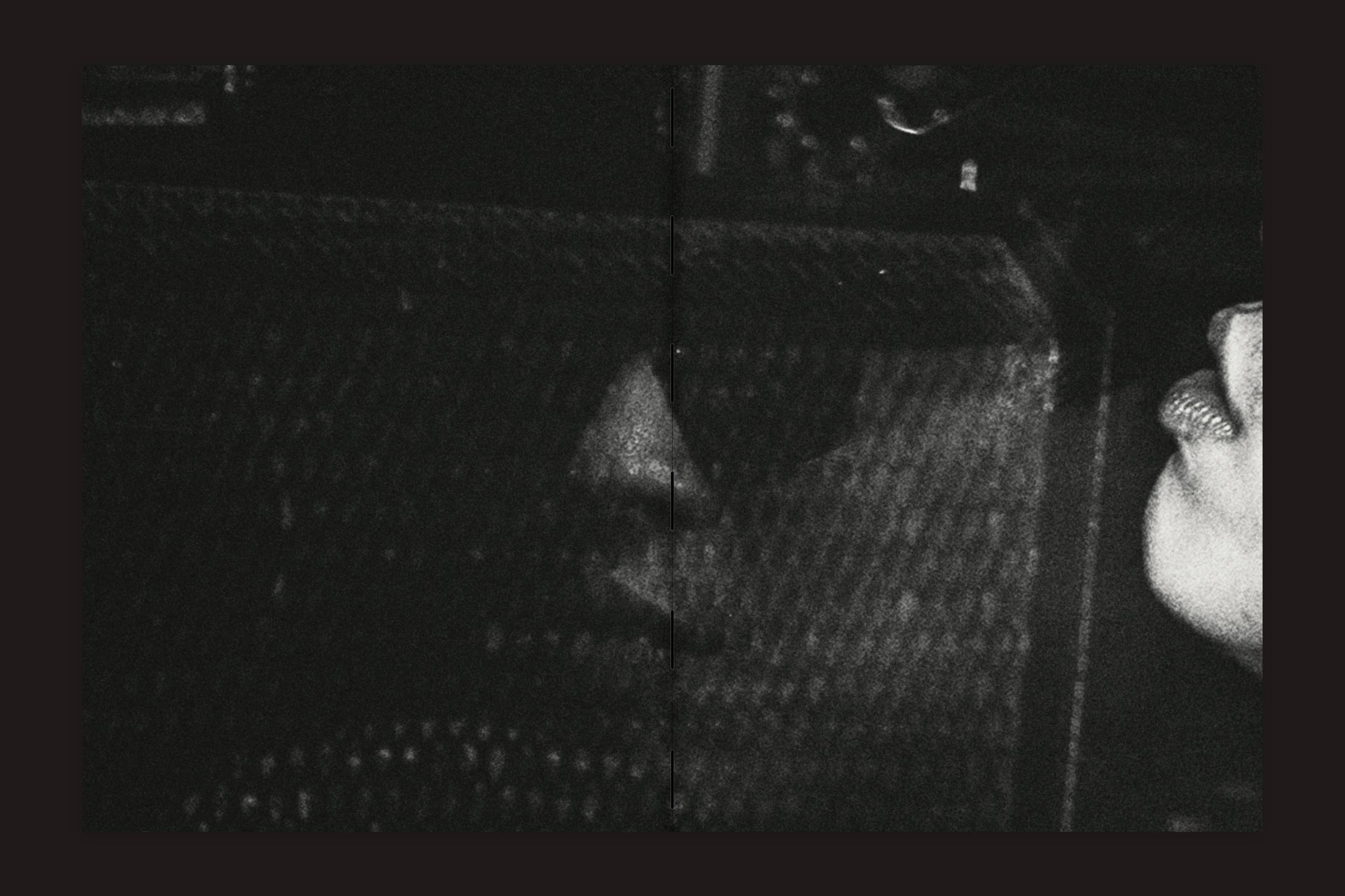 Close-up em preto e branco de uma pessoa de óculos escuros, com os lábios e o rosto parcialmente visíveis atrás de uma tela - um vislumbre enigmático de "Lucas Gibson: Shinsaibashi 2-18-9", de Selo Turvo.